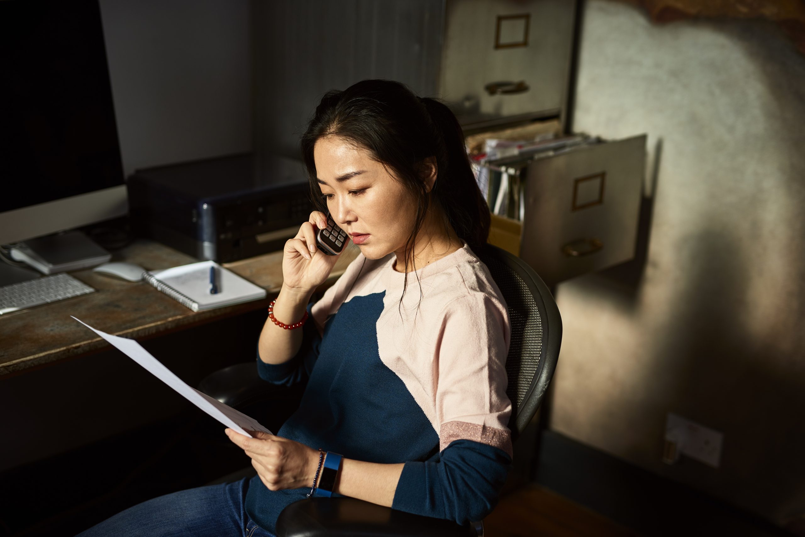 Portrait of Asian woman on cell phone reading important document