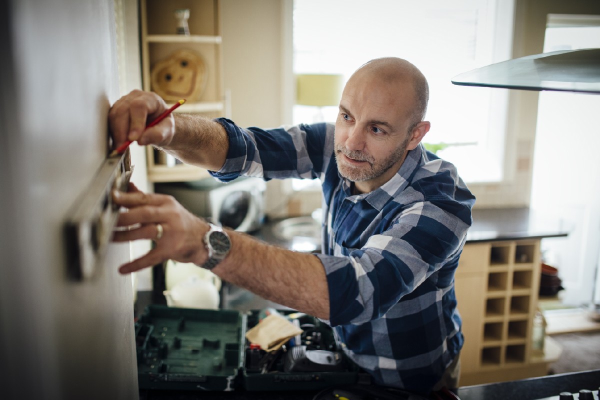 Mature man using a spirit level and marking the wall with a pencil in his kitchen.