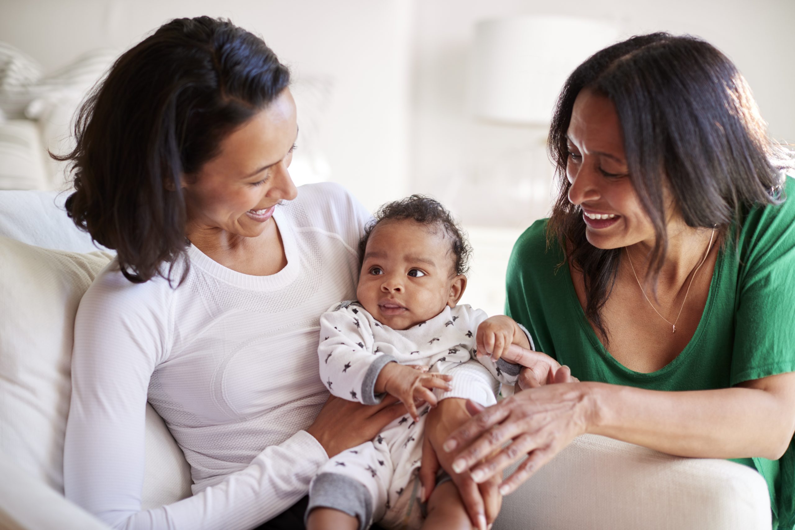 New mother sitting in an armchair holding her three month old baby son, with grandparent kneeling beside them