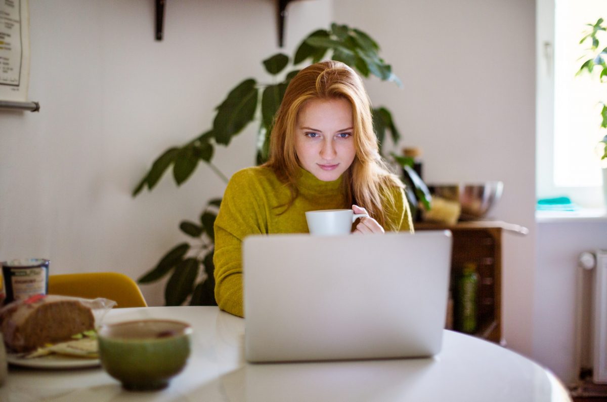 Woman drinking coffee and using laptop at home