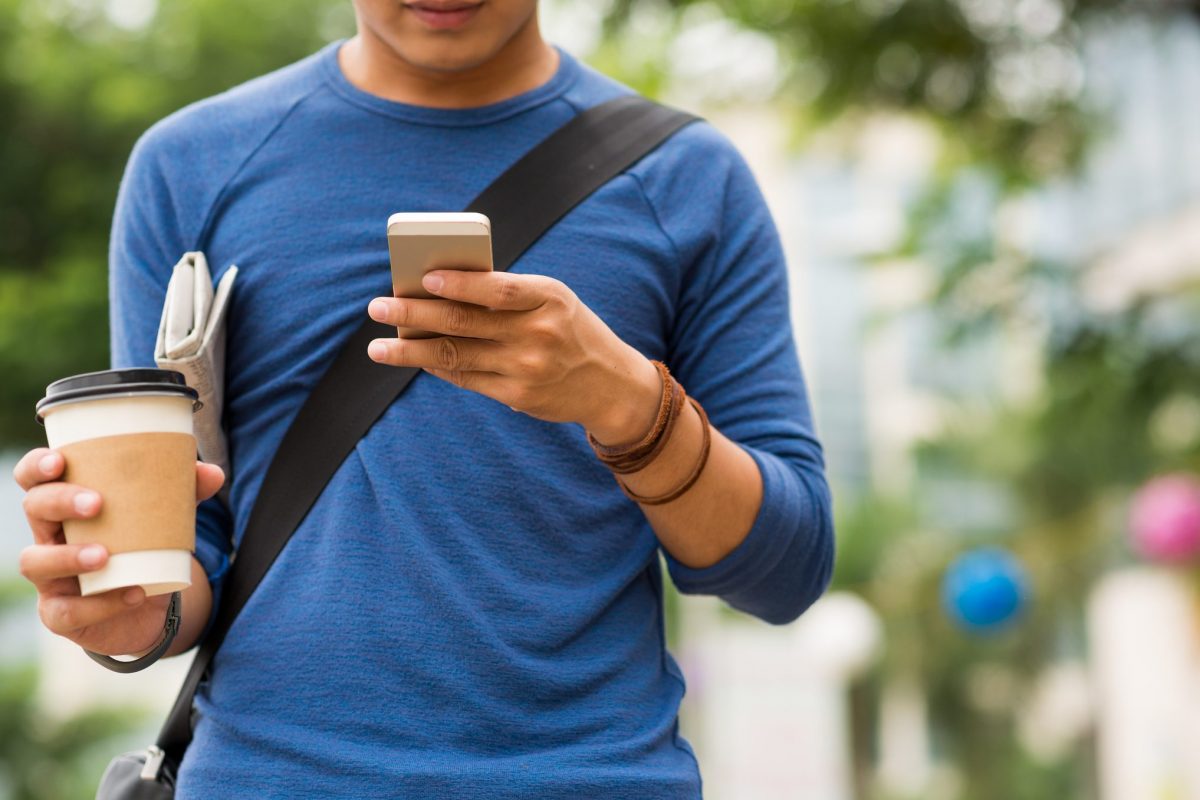 man-using-cellphone-holding coffee-while-walking-outside