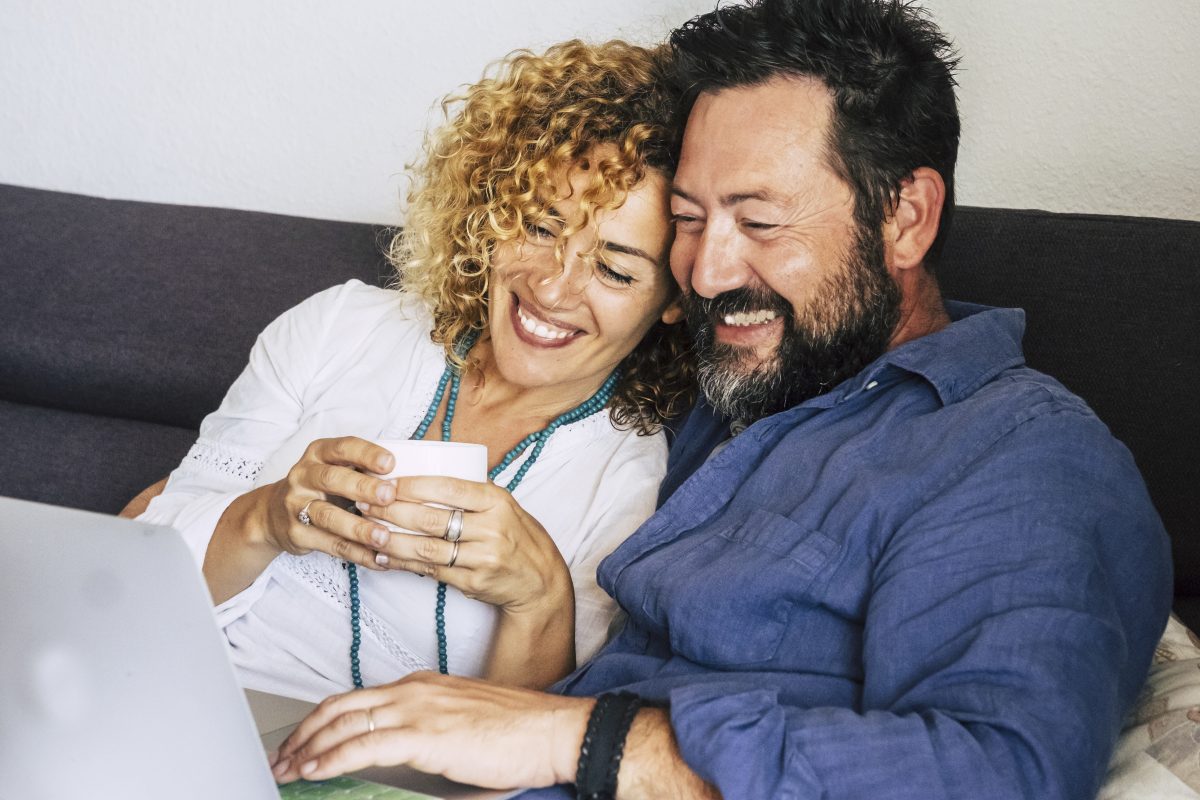 Happy couple sitting on the couch using laptop