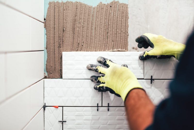 industrial construction worker installing small ceramic tiles on bathroom