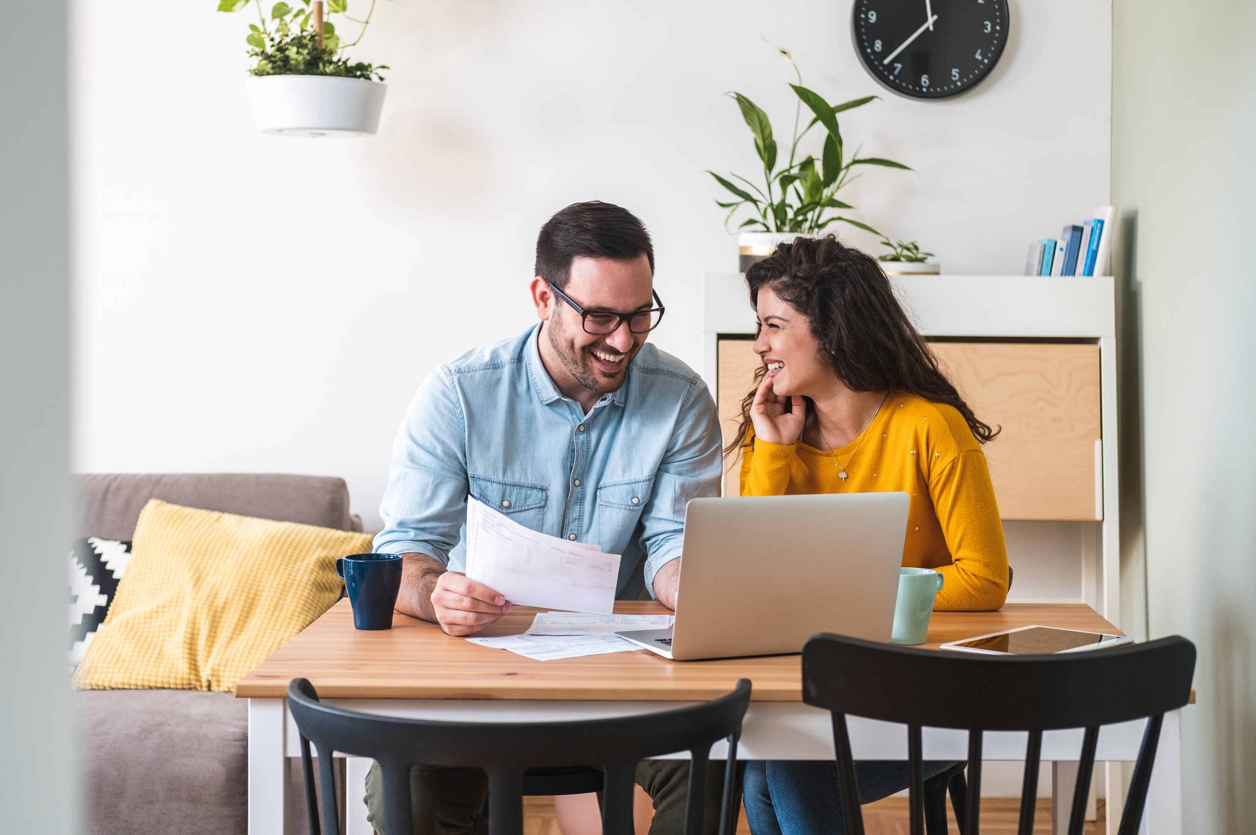 Happy husband and wife read good news online at laptop, smiling man holding documents receiving positive decision from mortgage broker